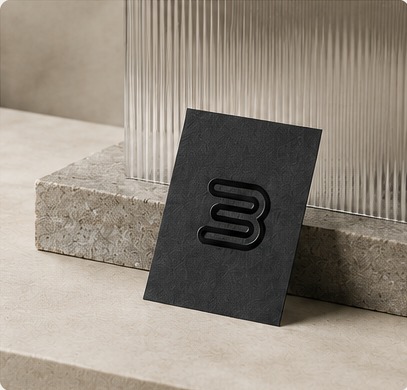 A black Brinkworks card standing upright against a ribbed glass panel on a stone plinth.